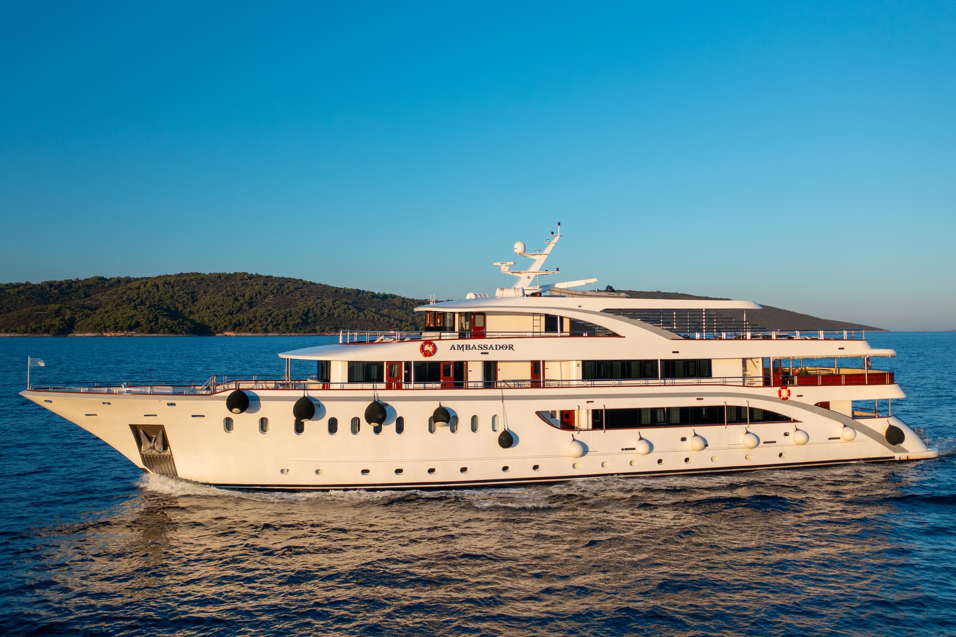 Ambassador luxury yacht cruising on calm sea water near forested coastline