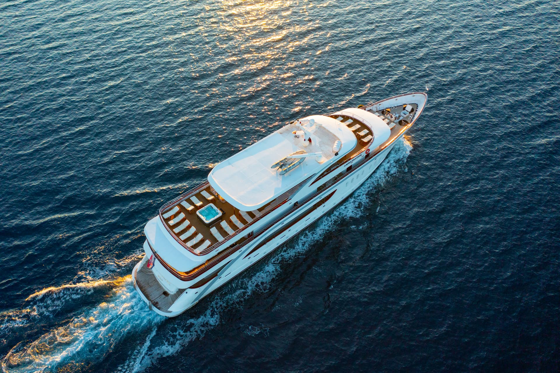 Aerial view of large white yacht cruising on blue sea water at sunset