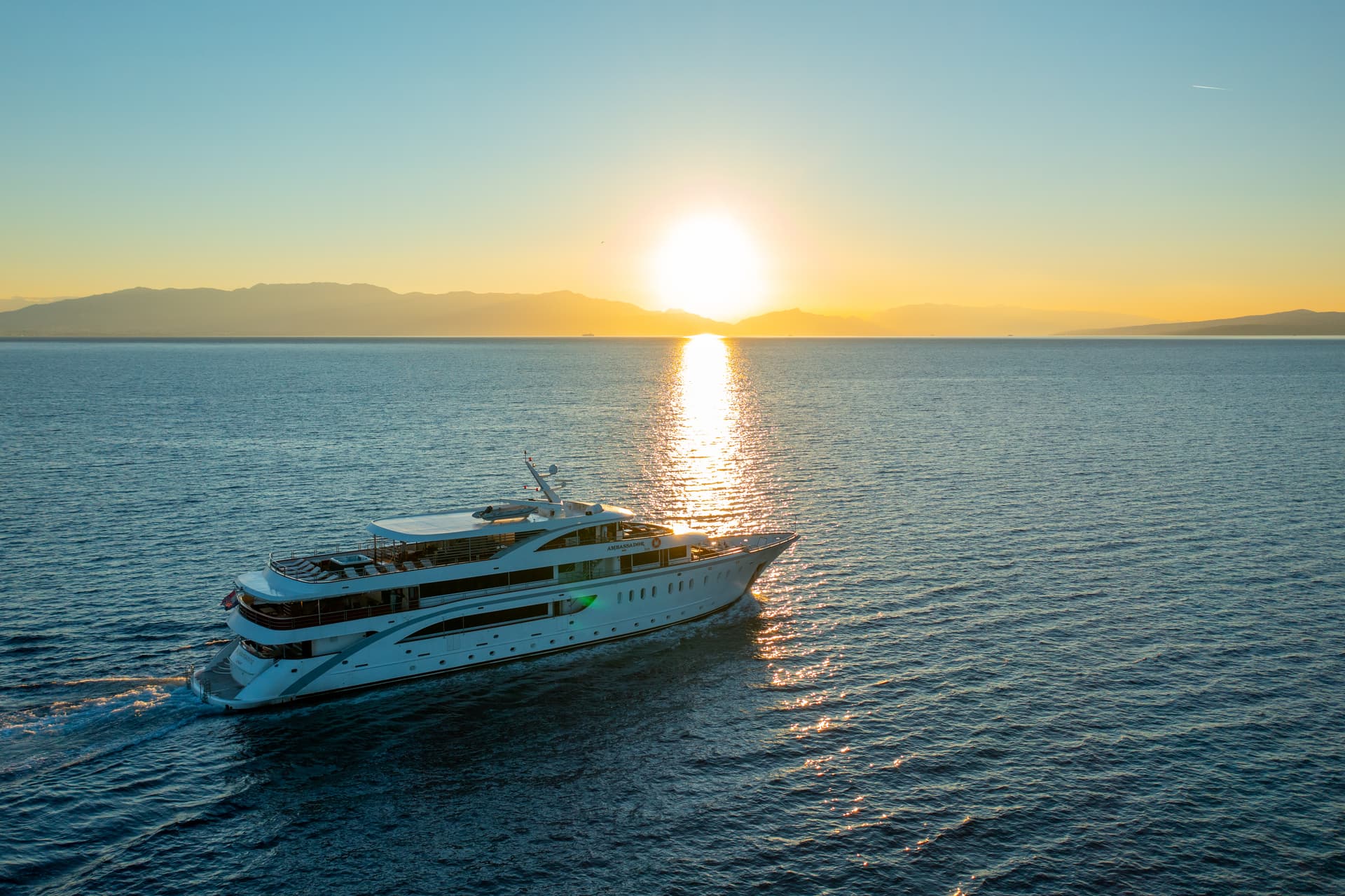 Large white yacht cruising on calm sea at sunset with distant mountains
