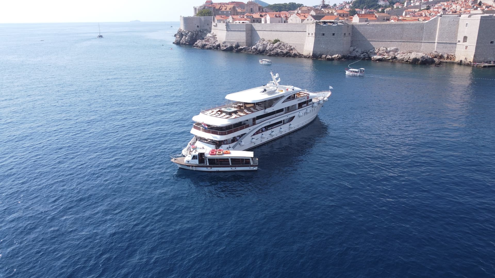 Large white yacht anchored near historic stone city walls by blue sea