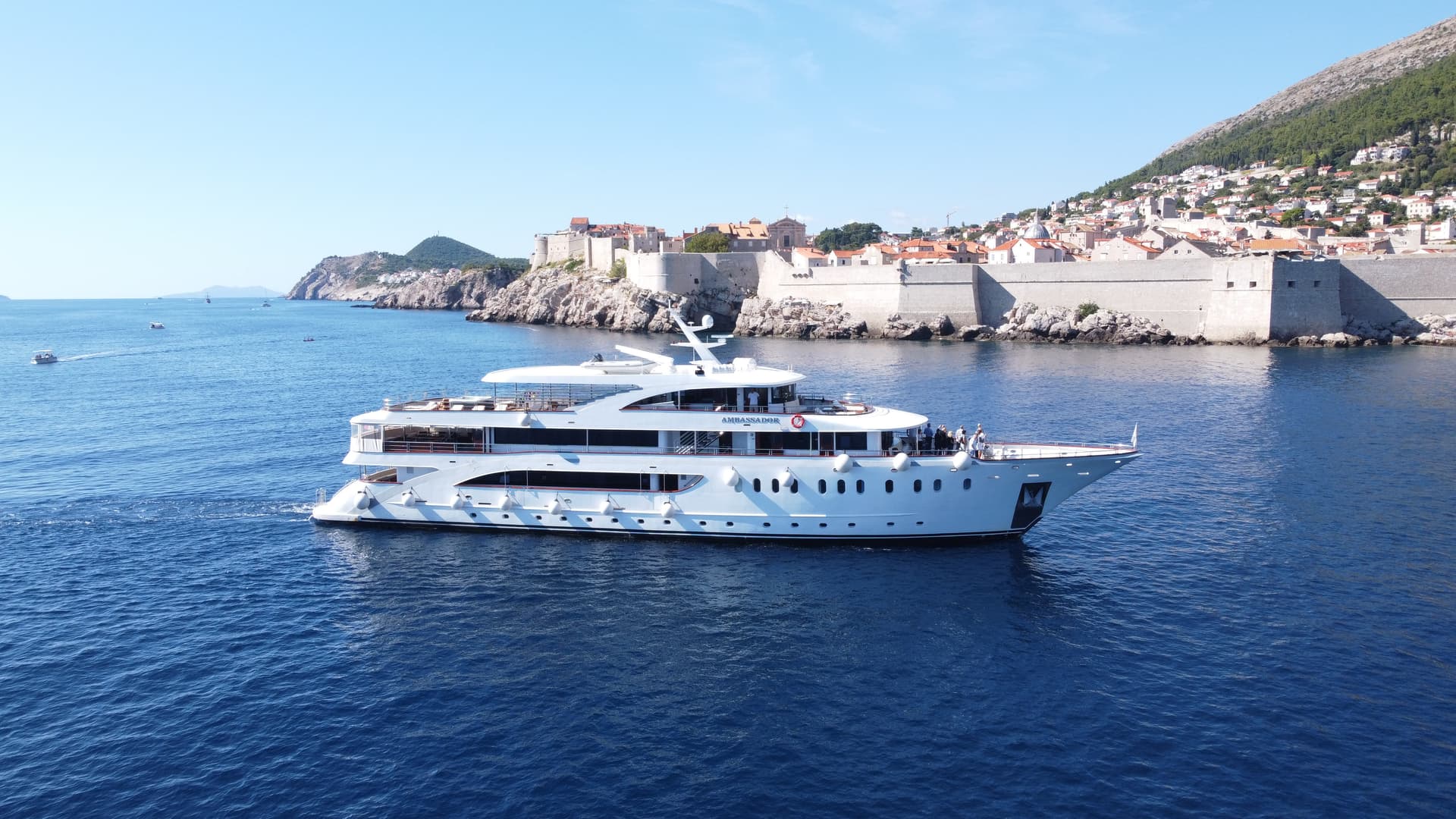 White yacht cruising on blue coastal waters near a historic walled city