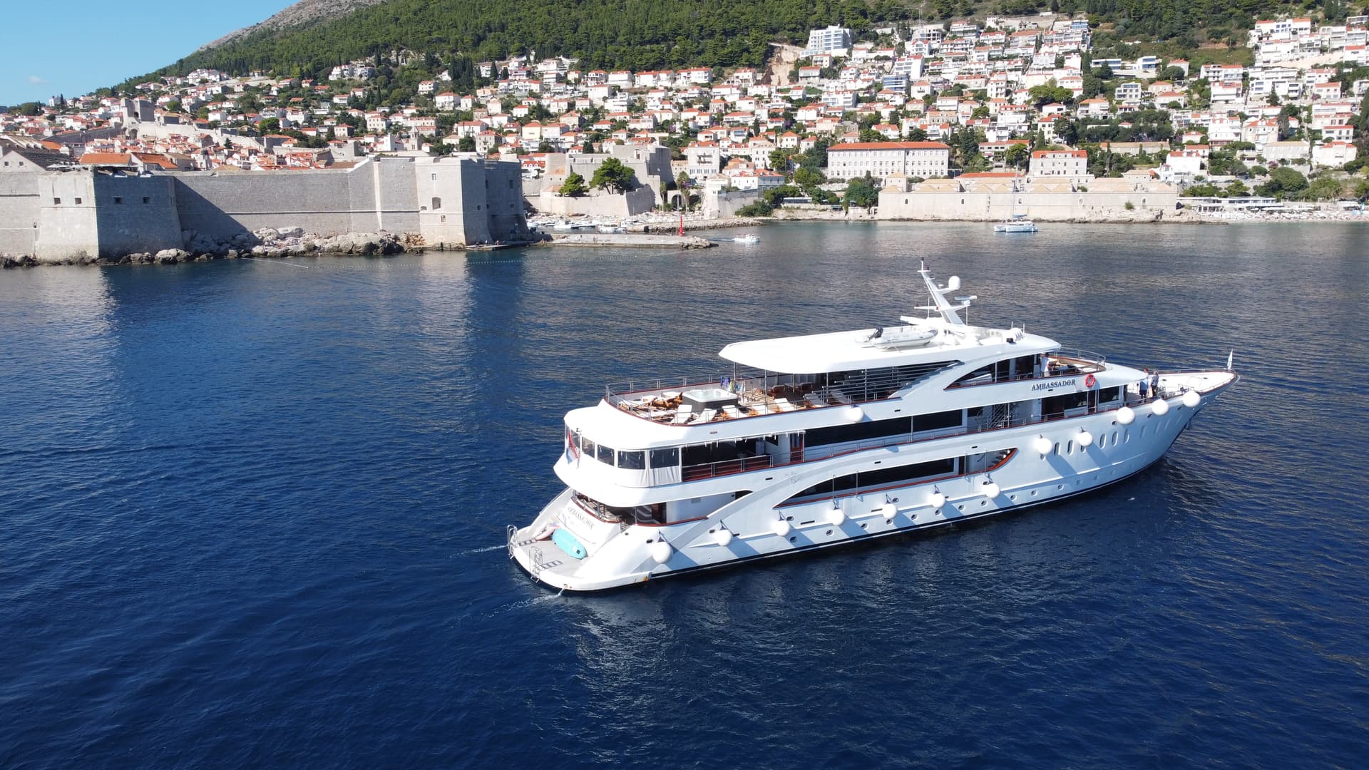 White luxury yacht cruising on blue water near a coastal city with historic stone walls