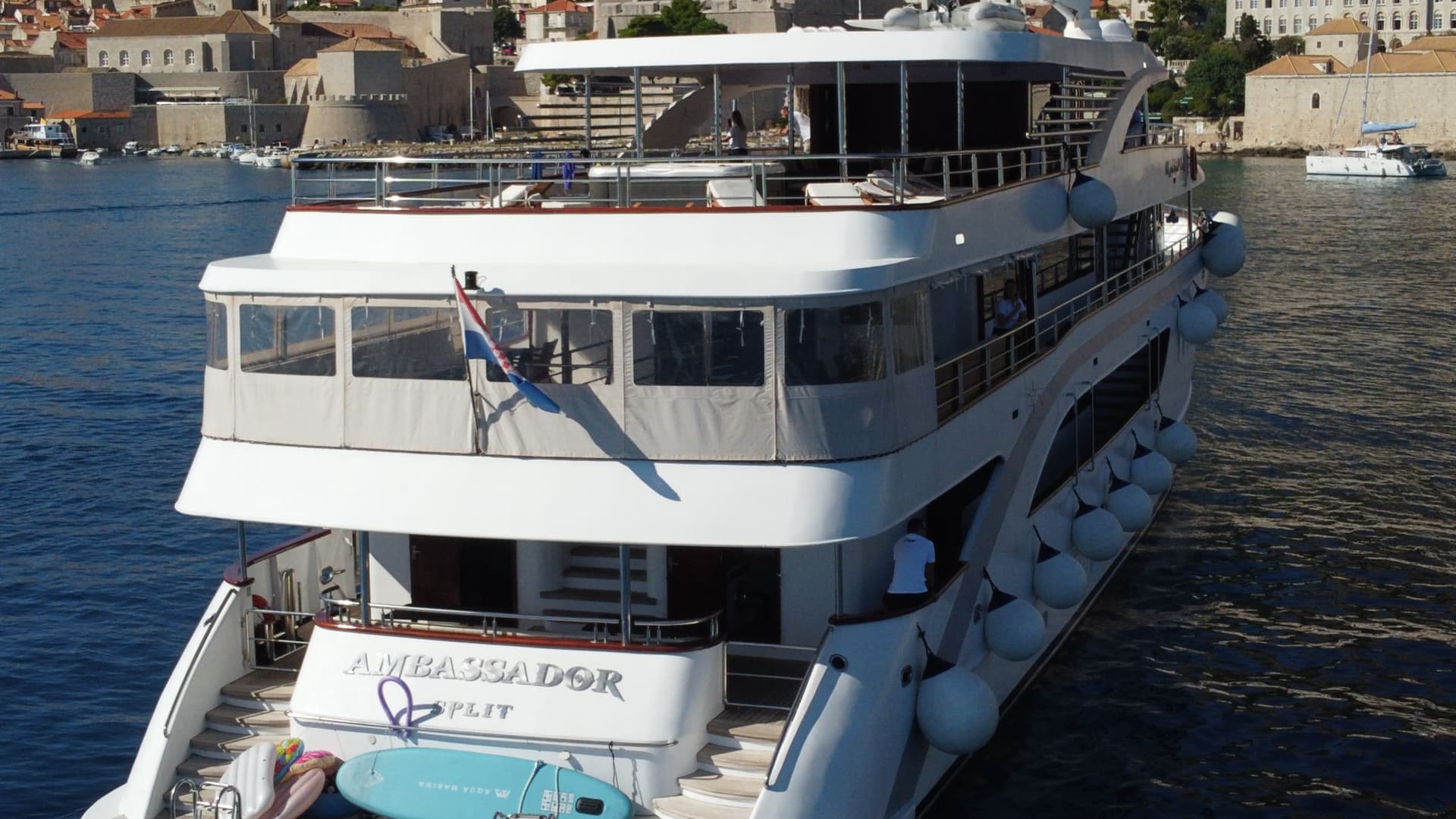 Large white yacht with multiple decks docked in harbor near historic stone buildings