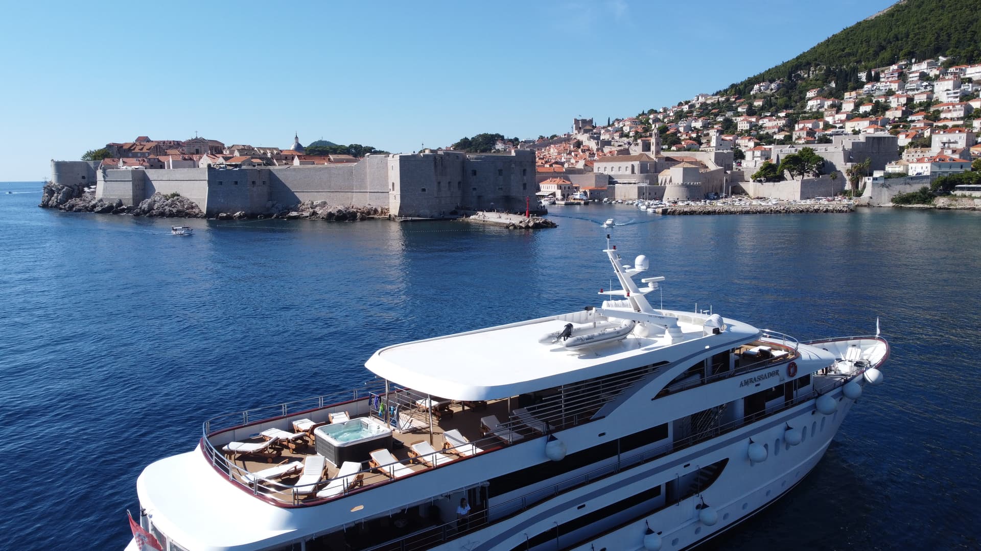 White yacht on blue coastal water with historic fortress city in background