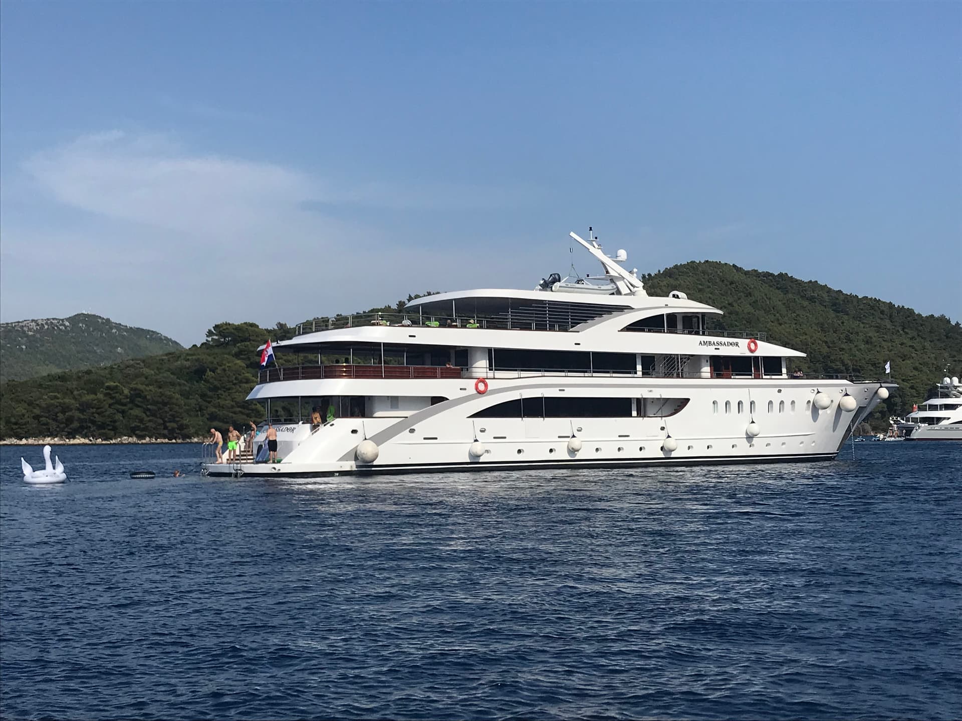 Large white yacht on blue coastal waters with green hills in background