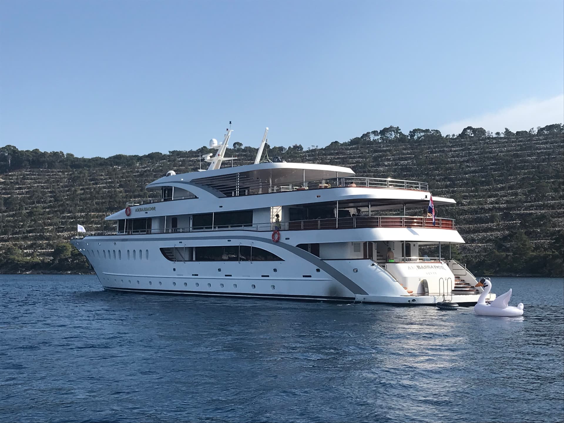 Large white yacht on blue coastal water with wooded hills in the background