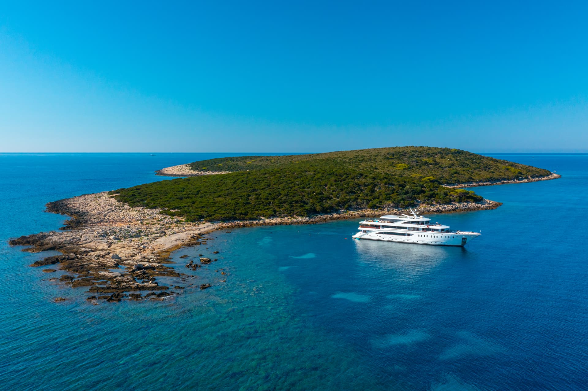 White yacht anchored near a green island in blue coastal waters