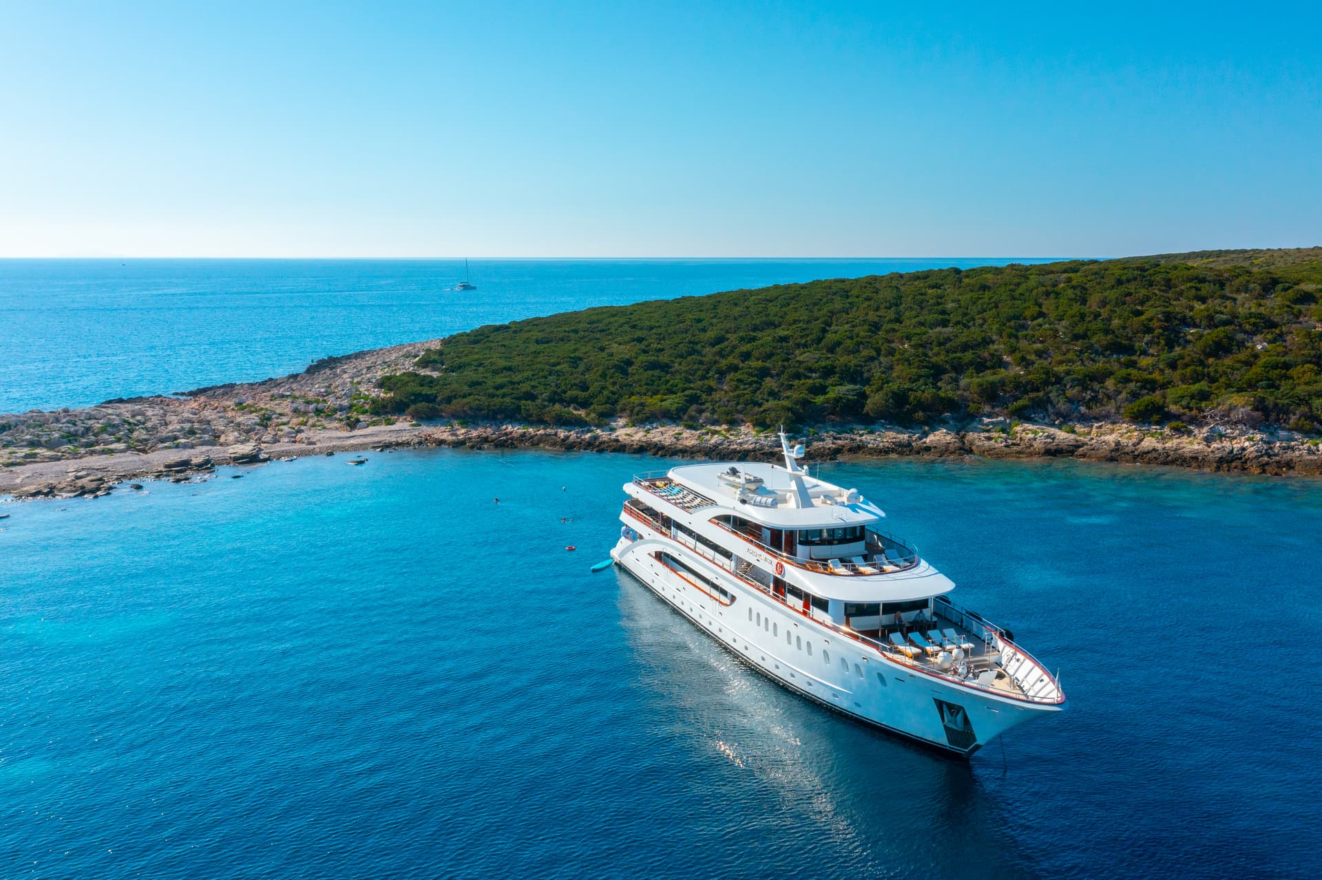 Large white yacht anchored in a turquoise bay near a forested coastline