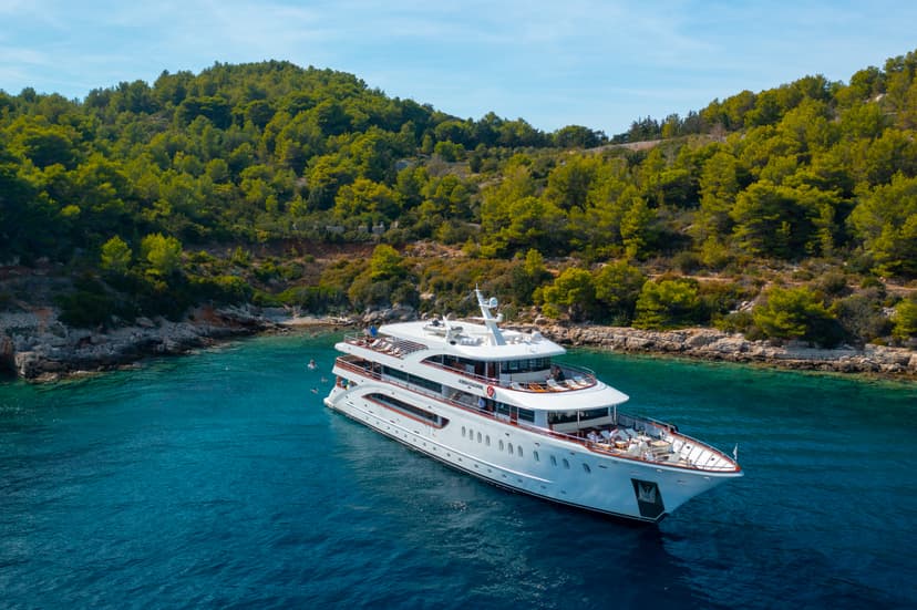 White yacht anchored in a coastal cove with blue water and green forested hills