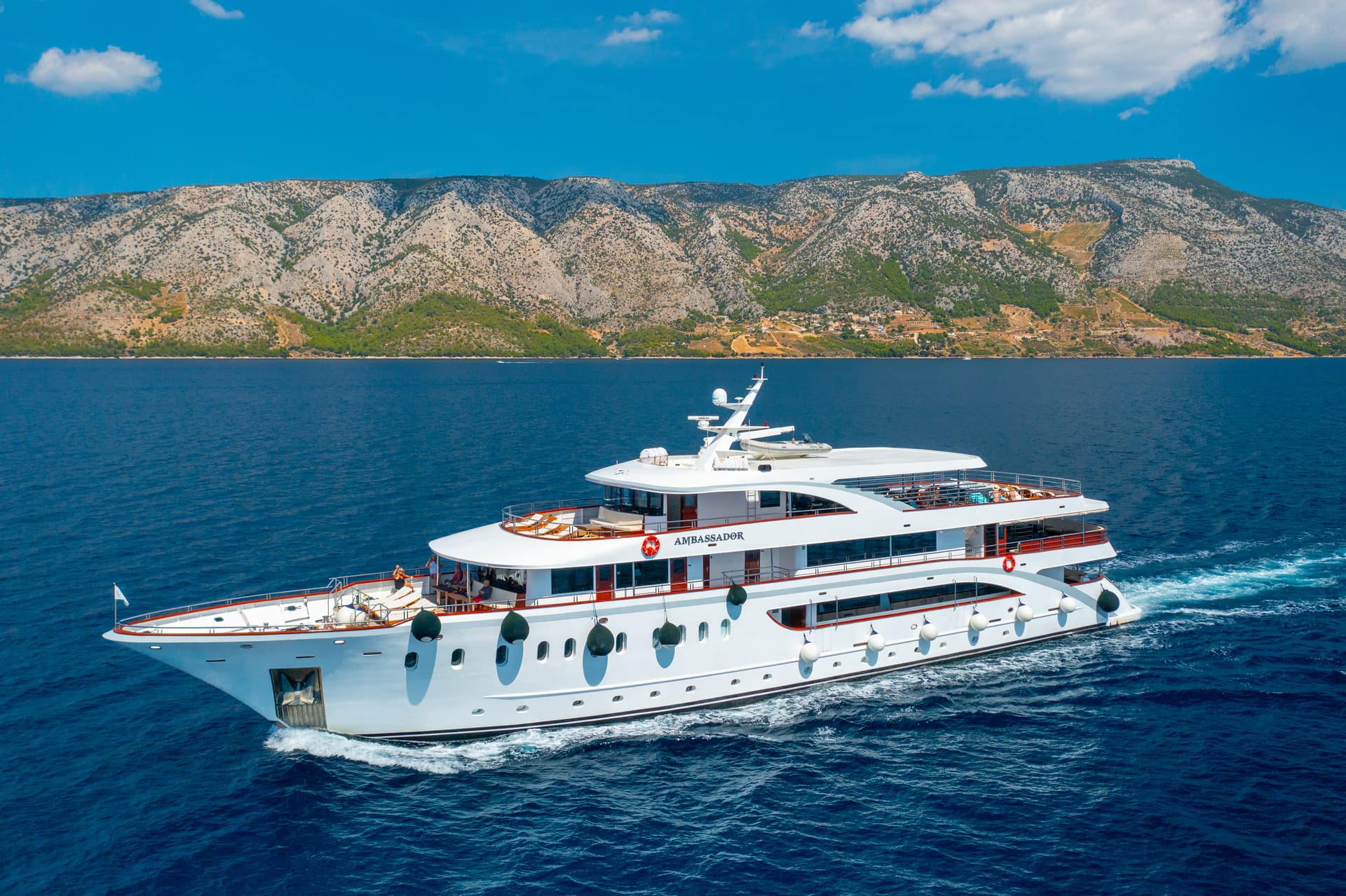 Luxury yacht Ambassador cruising on blue sea before mountain coastline