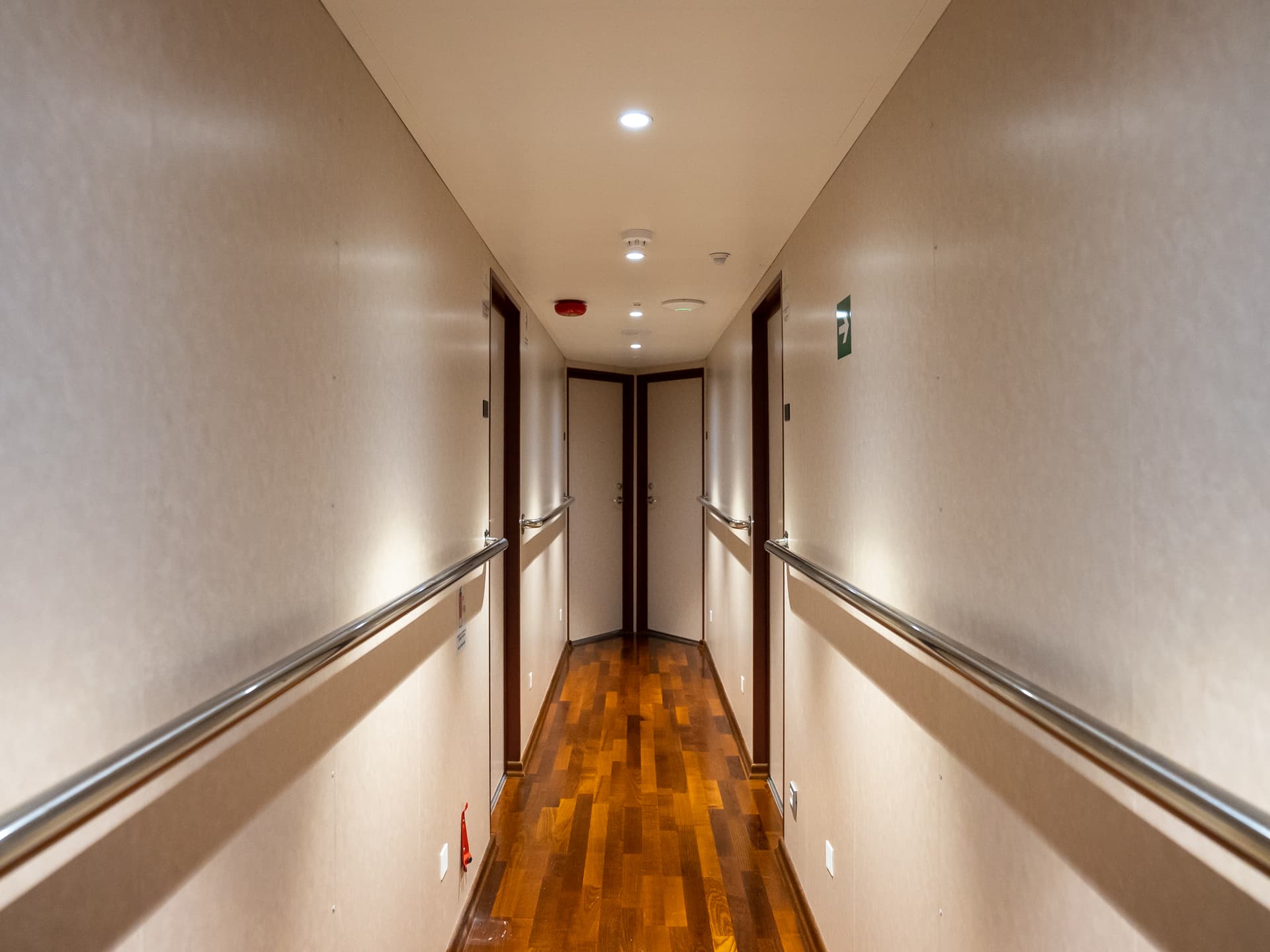 Narrow hotel or ship hallway with wood flooring and handrails along walls