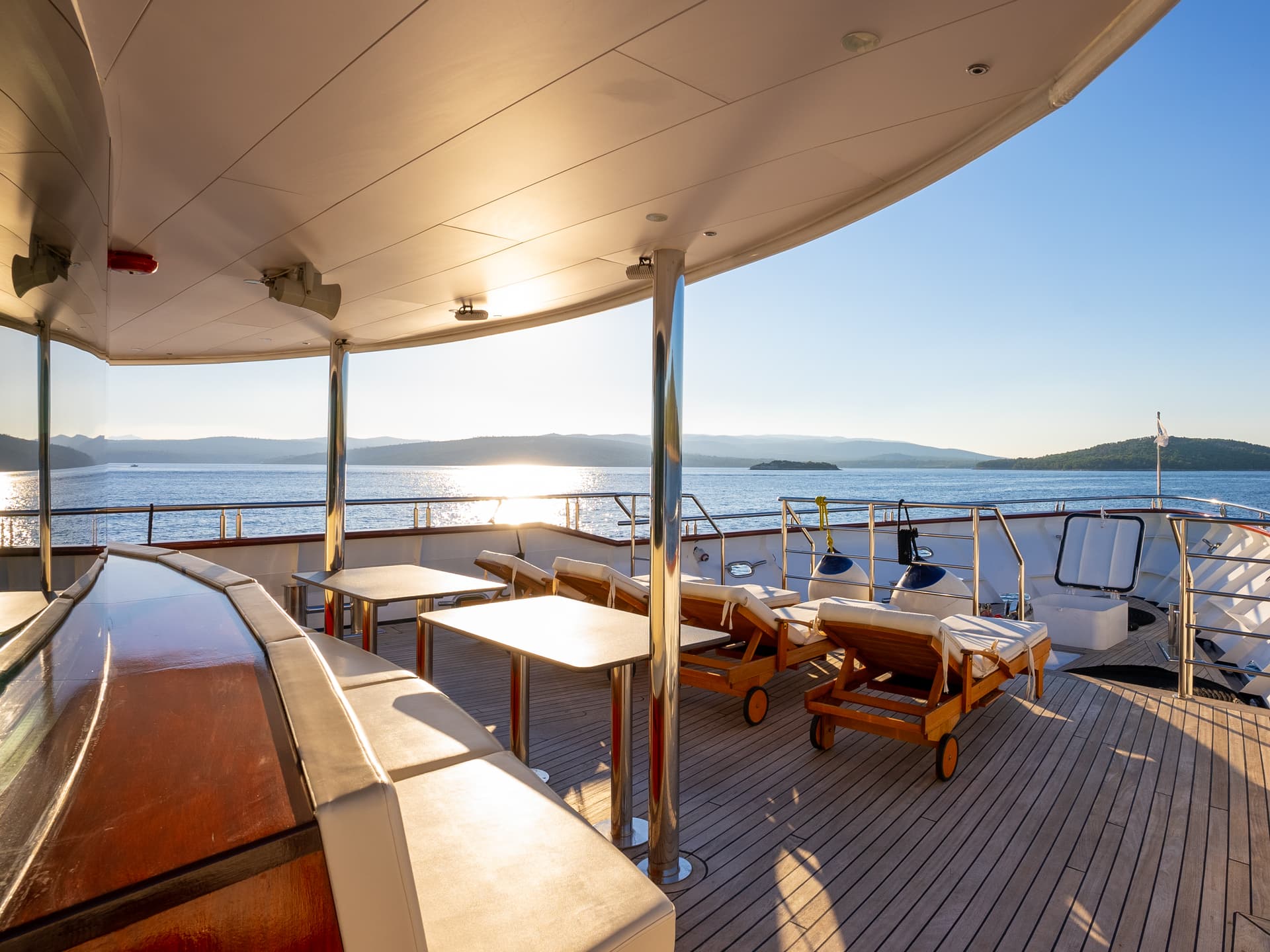 Yacht deck with tables, lounge chairs, and seating overlooking coastal waters at sunset