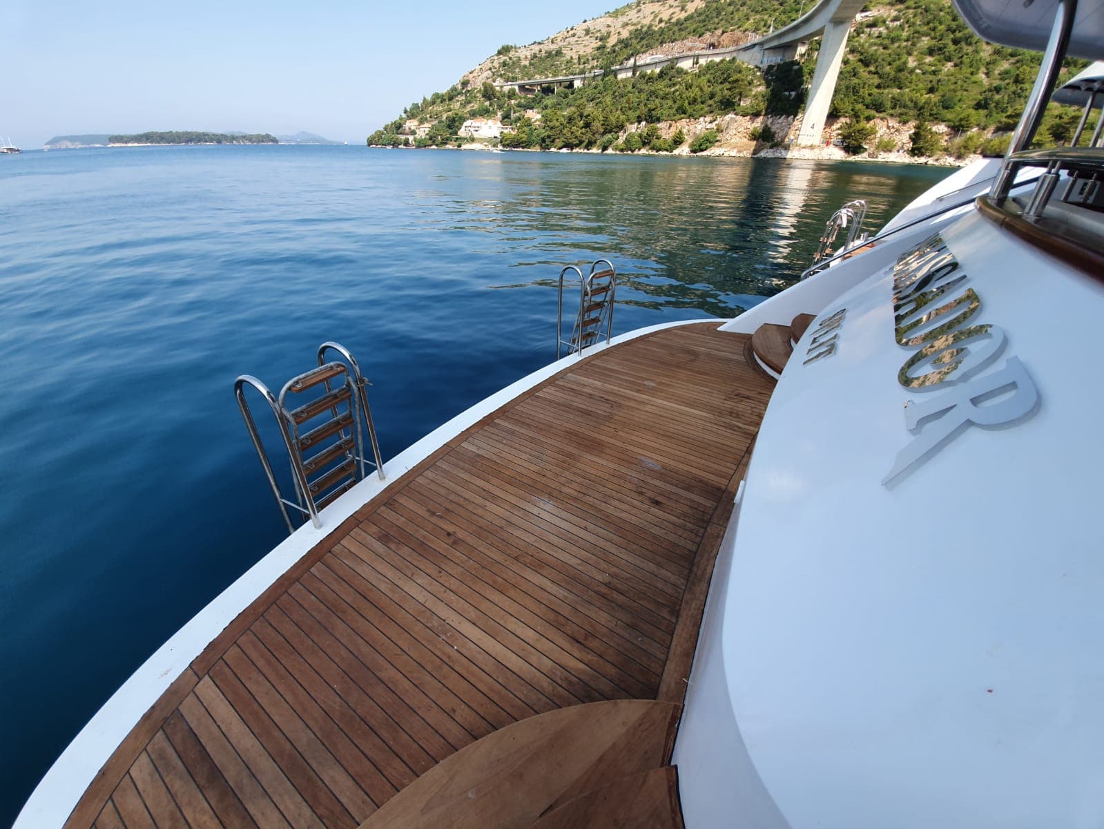 Yacht stern deck with wooden platform and swim ladders on calm blue coastal waters