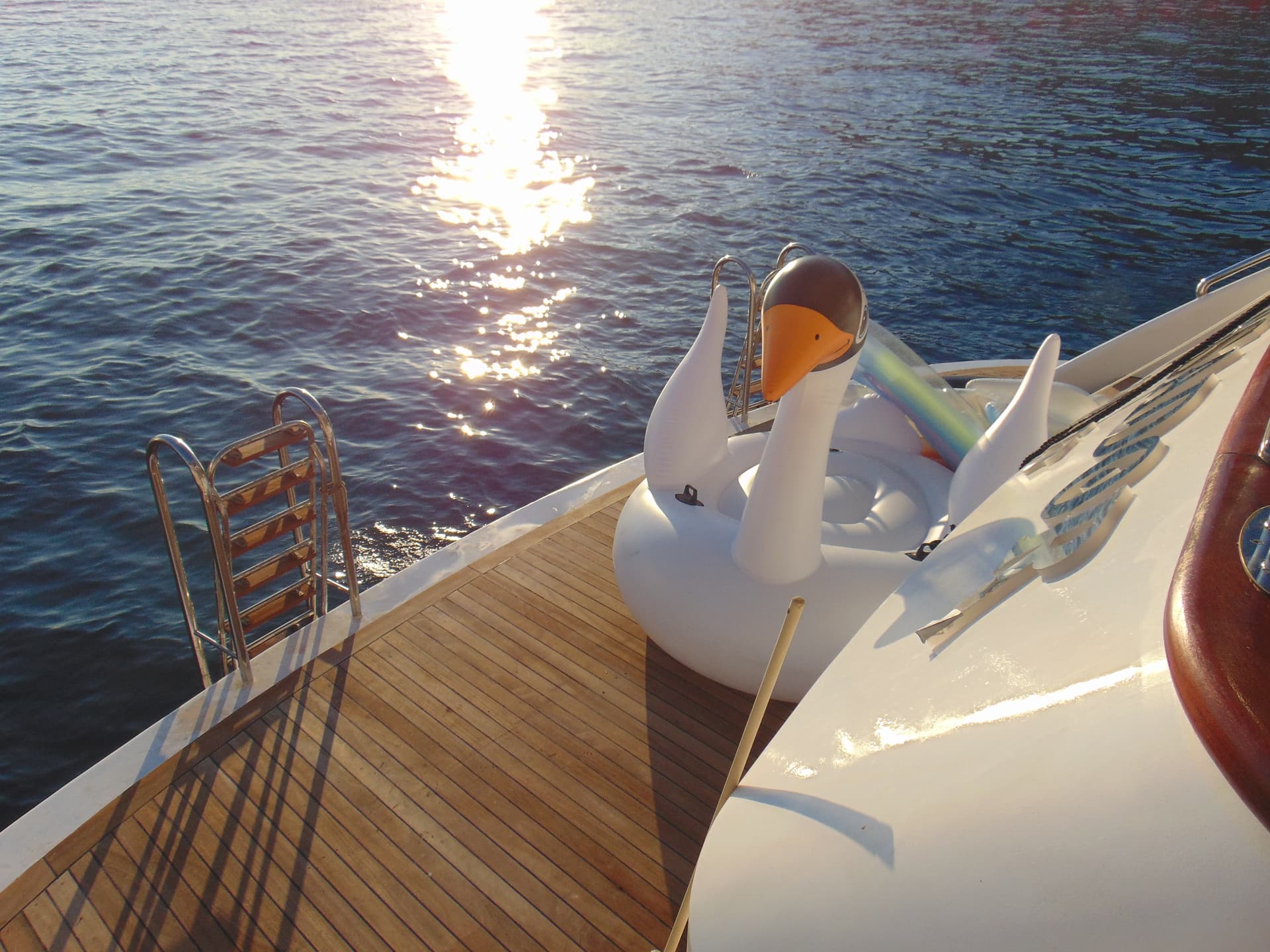 Inflatable swan float on the wooden deck of a yacht with sunlight reflecting on the water