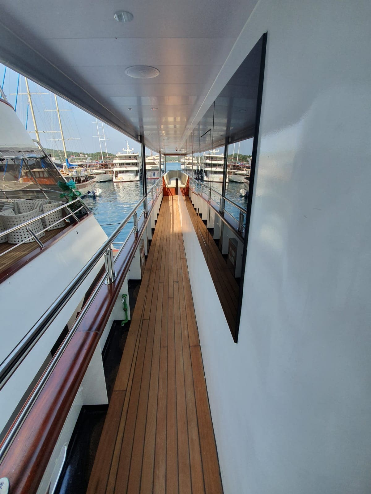 Wooden deck walkway along yacht side with view of harbor filled with boats