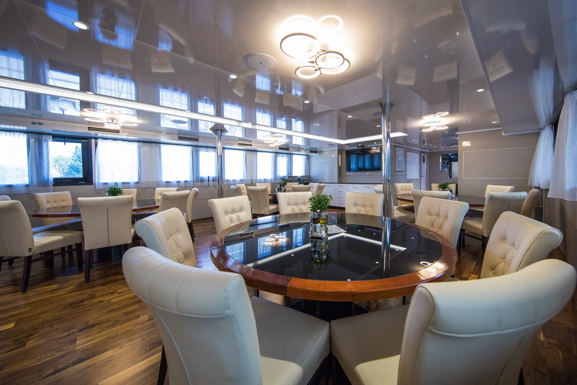 Modern restaurant interior with round dining tables and upholstered white chairs on wooden flooring.