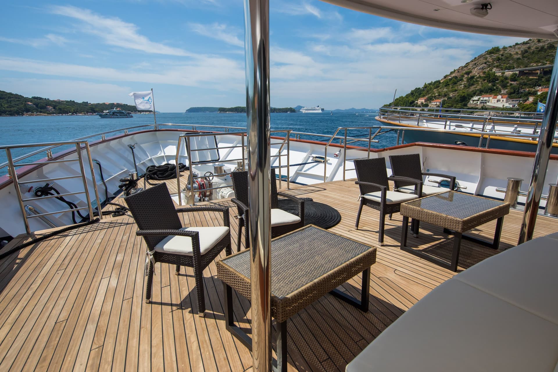 Sunny wooden deck of a yacht with seating and coastal view