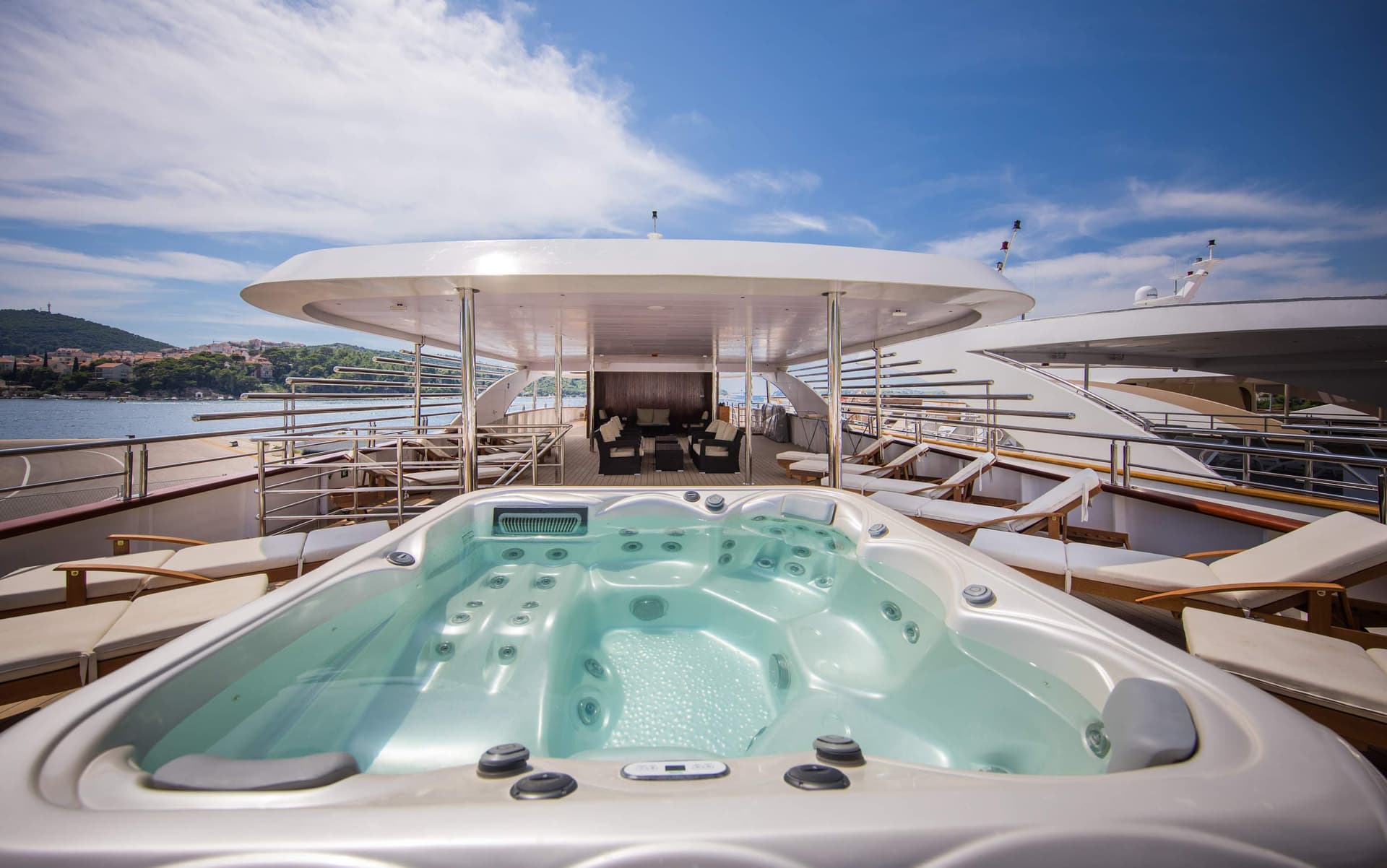 Luxury yacht sun deck with jacuzzi, lounge chairs, and shaded seating area overlooking the sea.