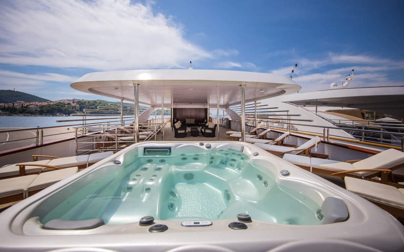 Luxury yacht sun deck with jacuzzi, lounge chairs, and shaded seating area overlooking the sea.