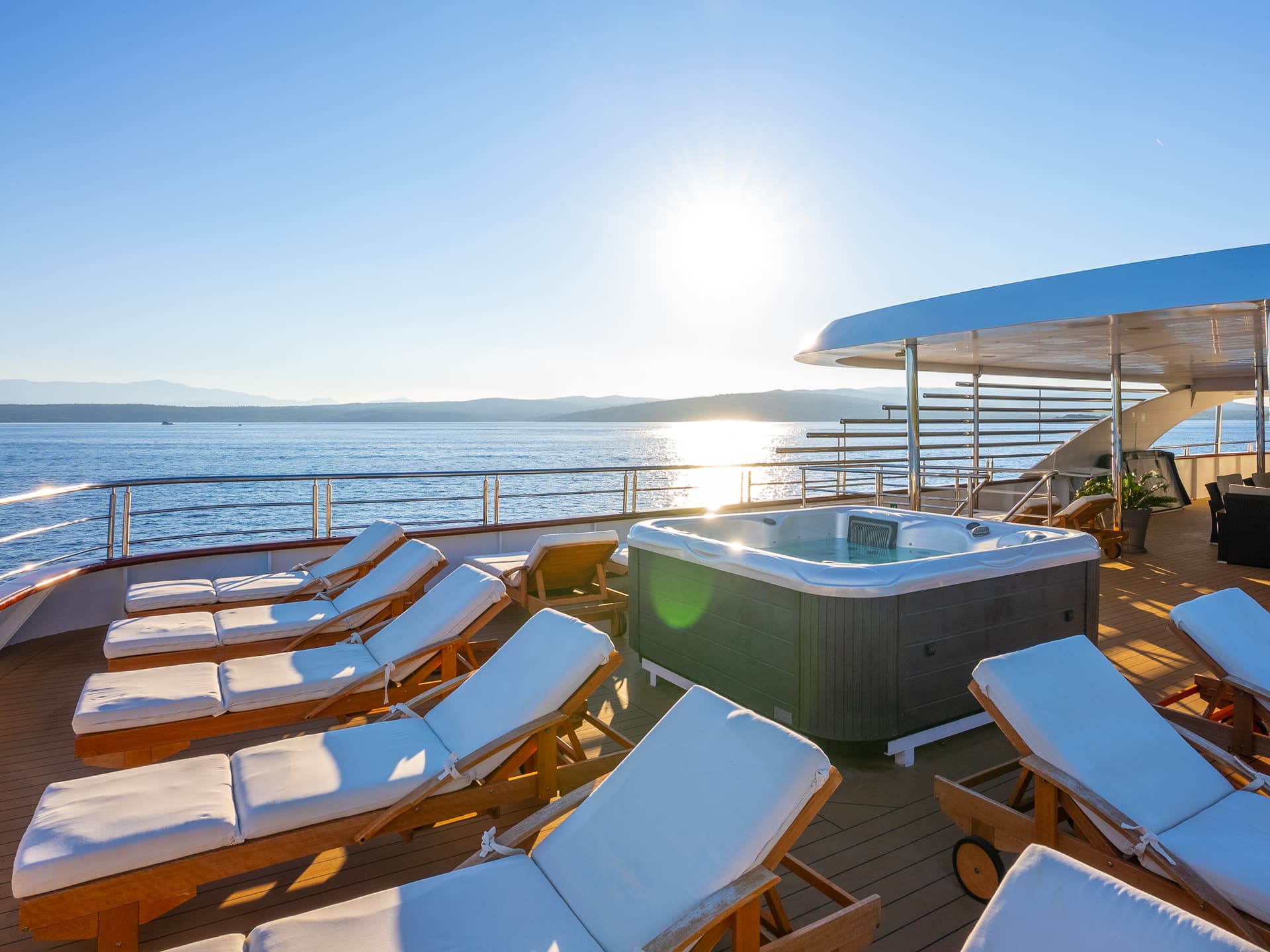 Yacht sun deck with hot tub and lounge chairs overlooking the sea on a sunny day
