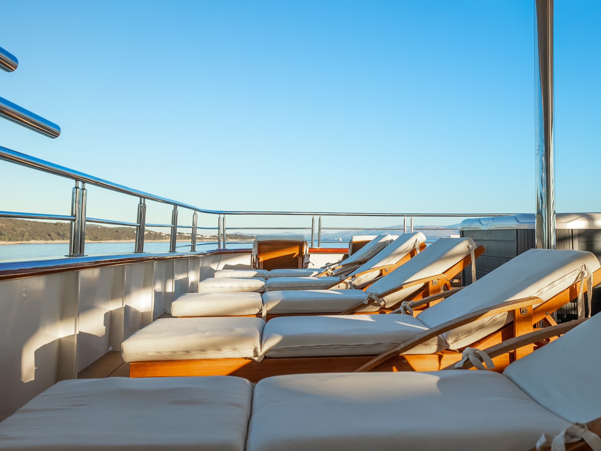 Sun loungers on the deck of a yacht with a view of the sea and coastline