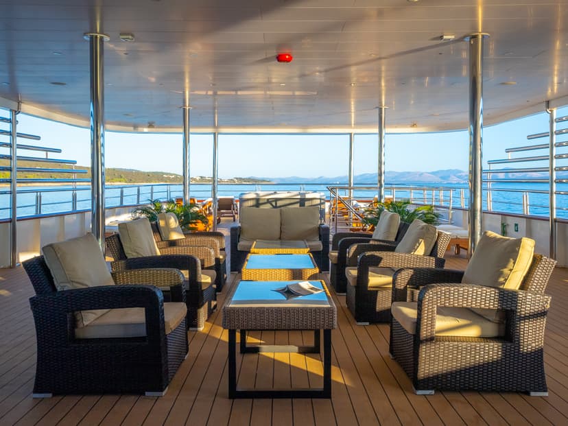 Sunny outdoor deck with wicker armchairs and tables on a boat with ocean views