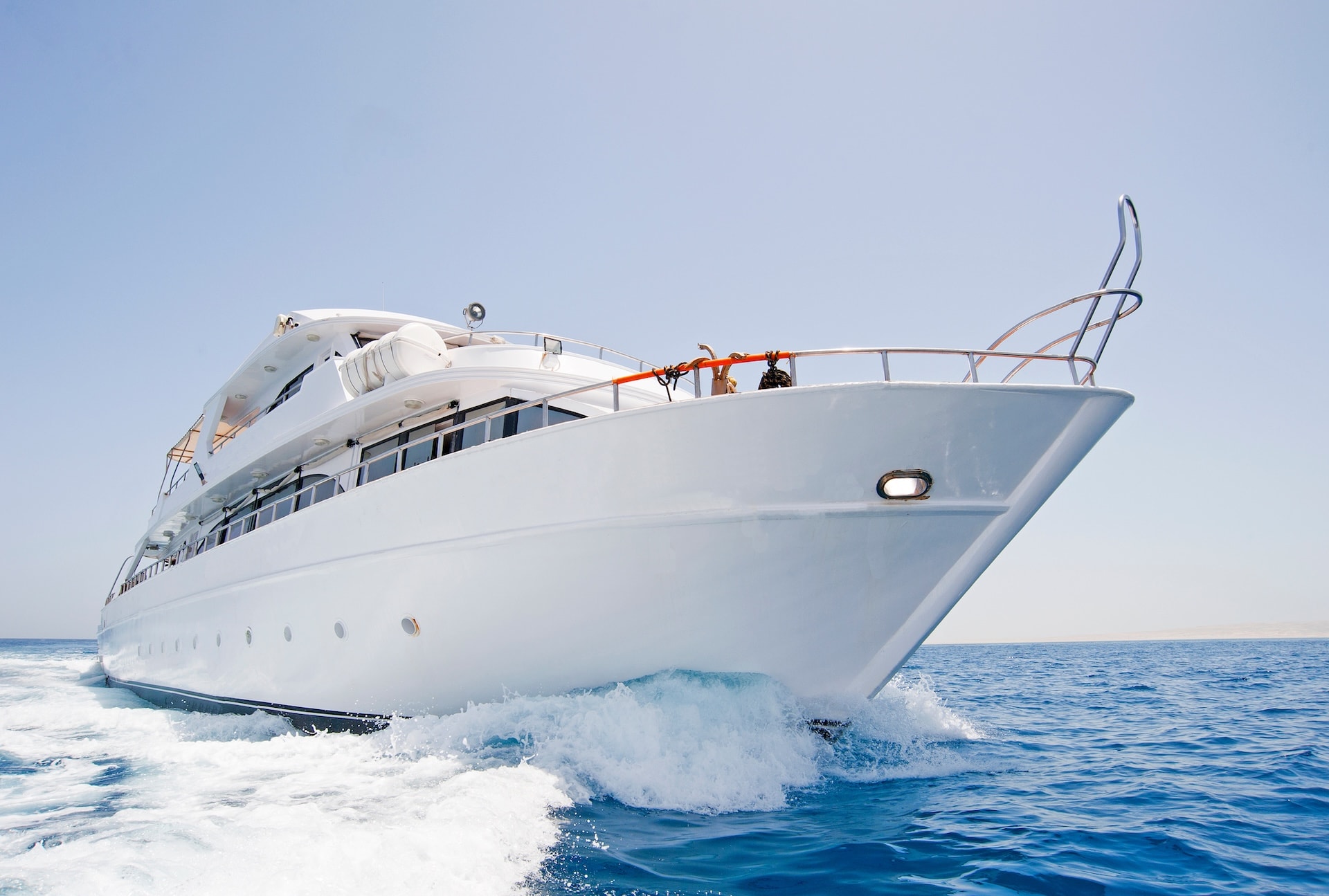 Large white yacht speeding through blue coastal waters under a clear sky