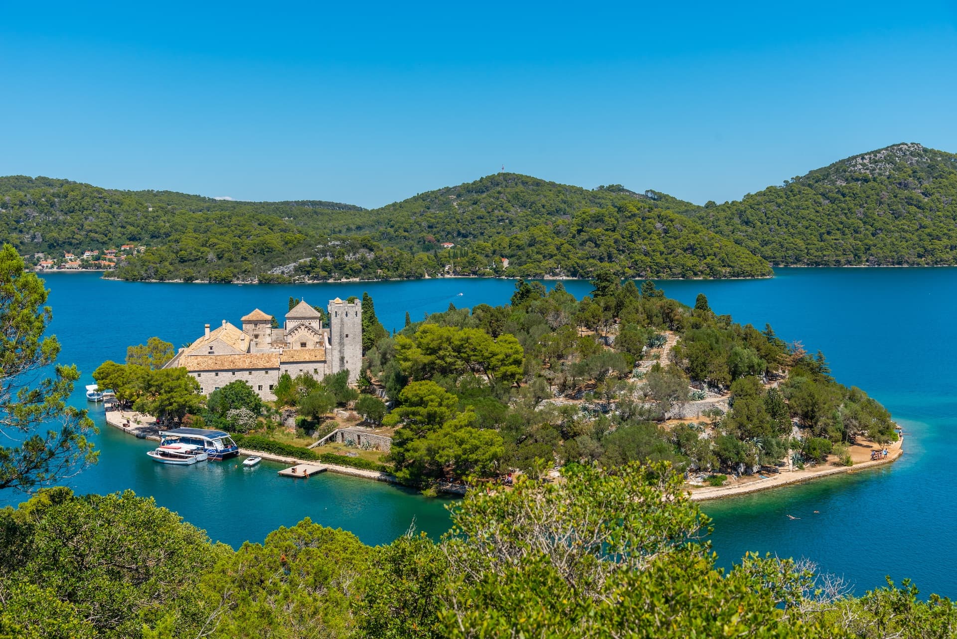 Mljet Island church on a wooded islet in bright blue water with forested hillsides.