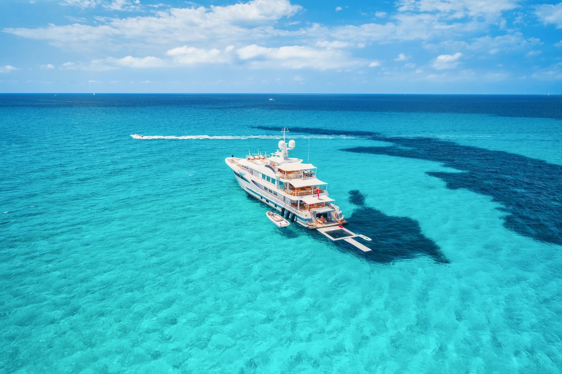 Large white motor yacht anchored in shallow turquoise water under a blue sky.