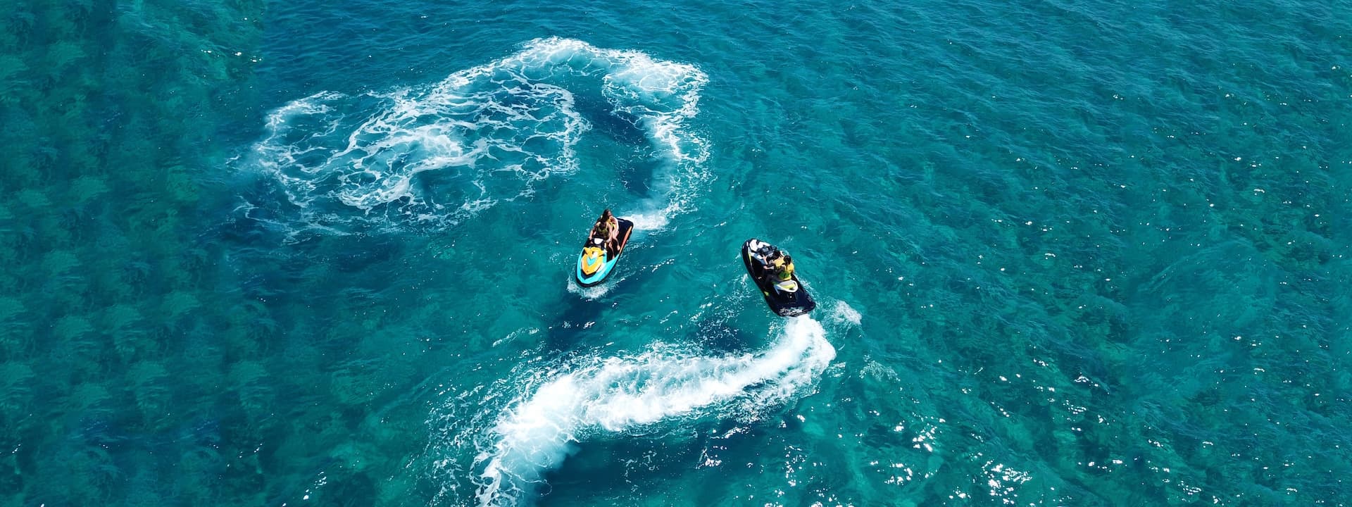 Two jet skis riding on clear turquoise water leaving white wakes, Brac.