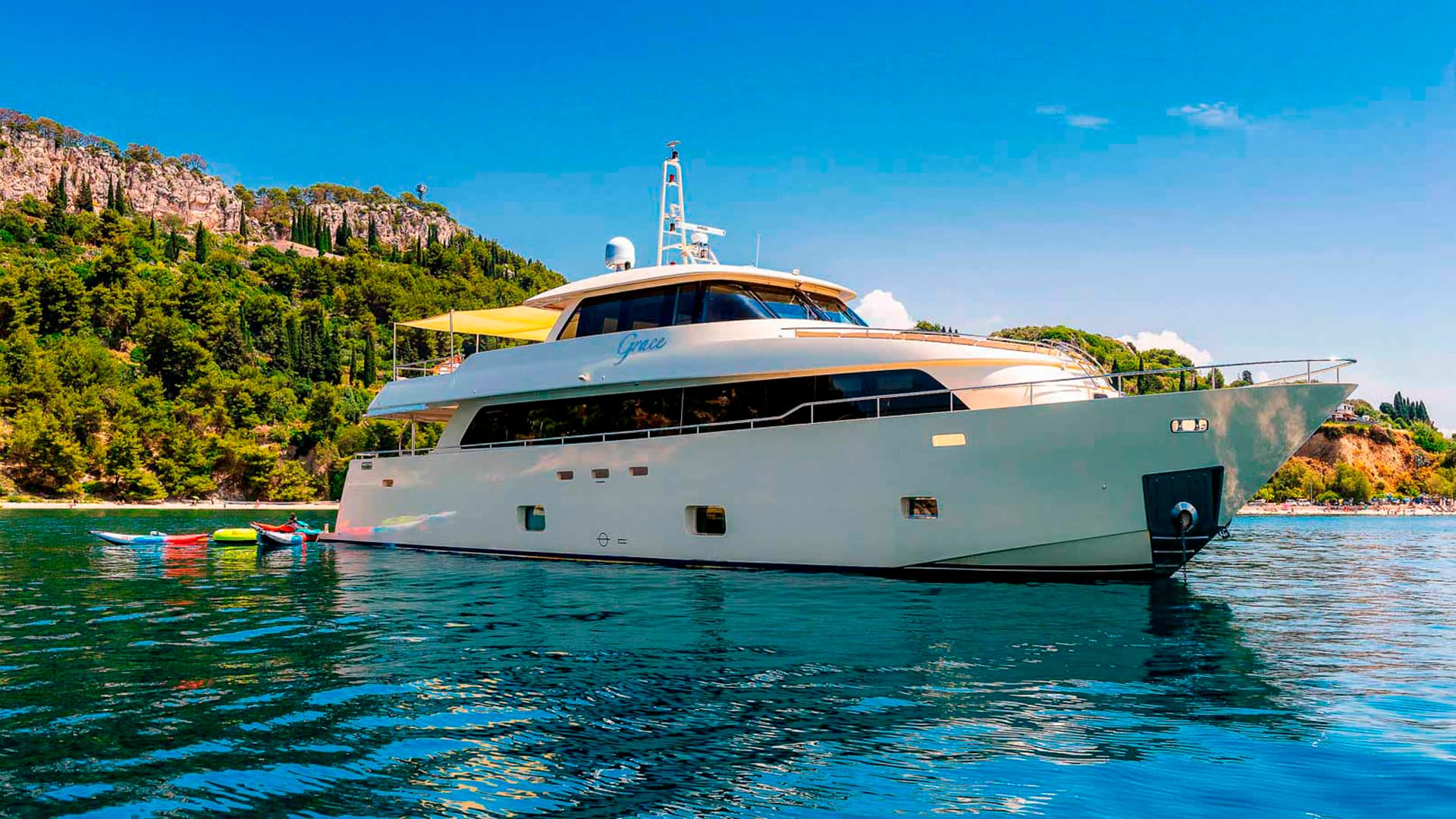 Motor yacht 'Grace' anchored in blue coastal waters near a lush, green hillside.