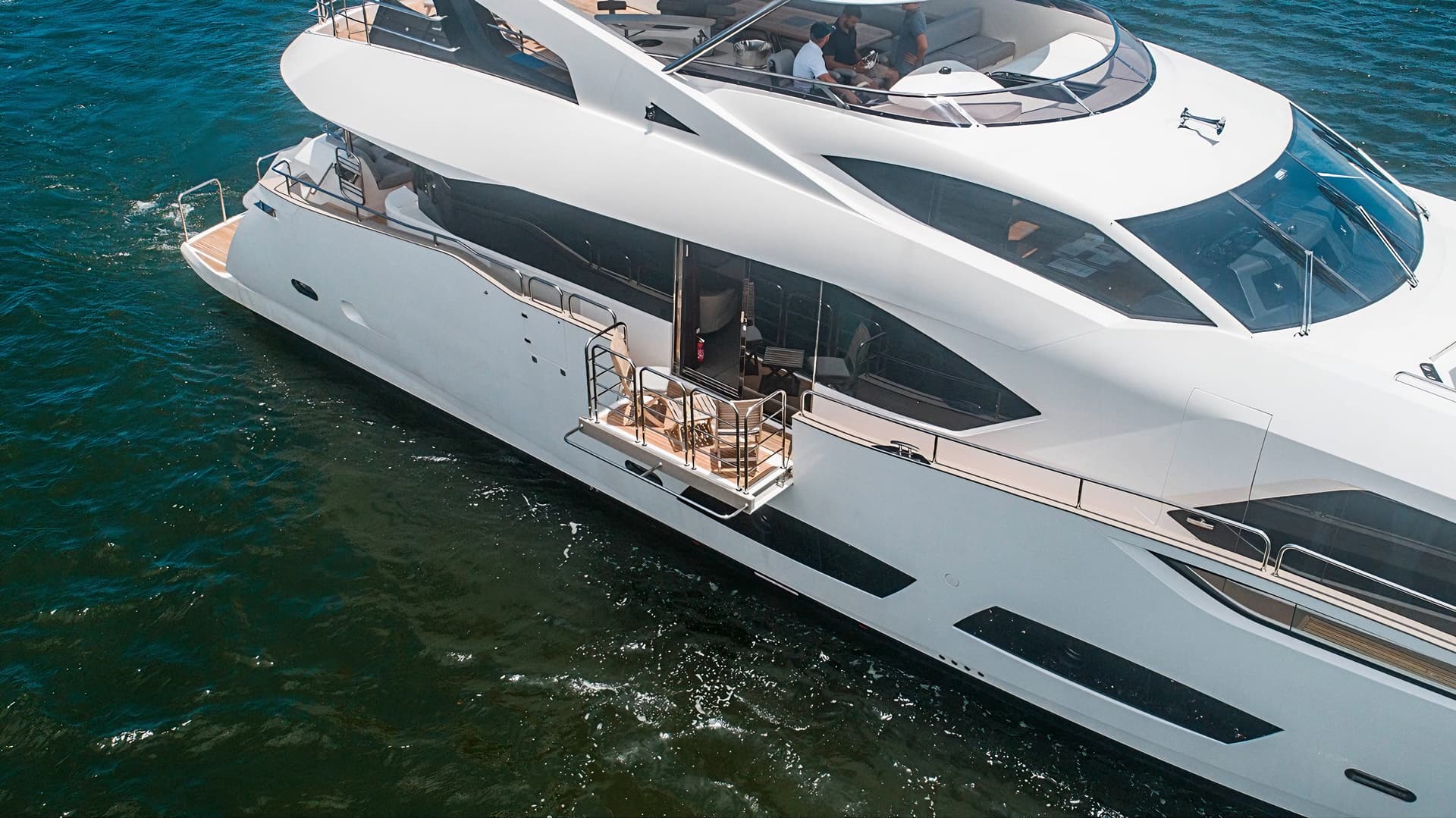 White luxury yacht cruising on dark green water with people visible on the upper deck.