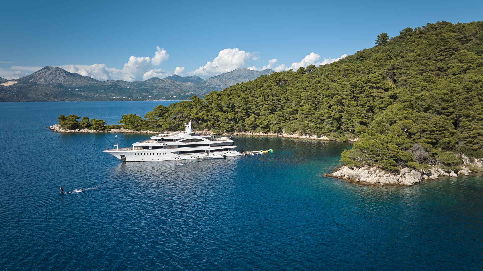Large white yacht anchored near forested coastline with mountains in background