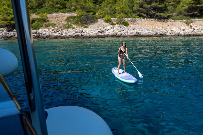 Person stand up paddleboarding on clear blue coastal waters near a rocky shore