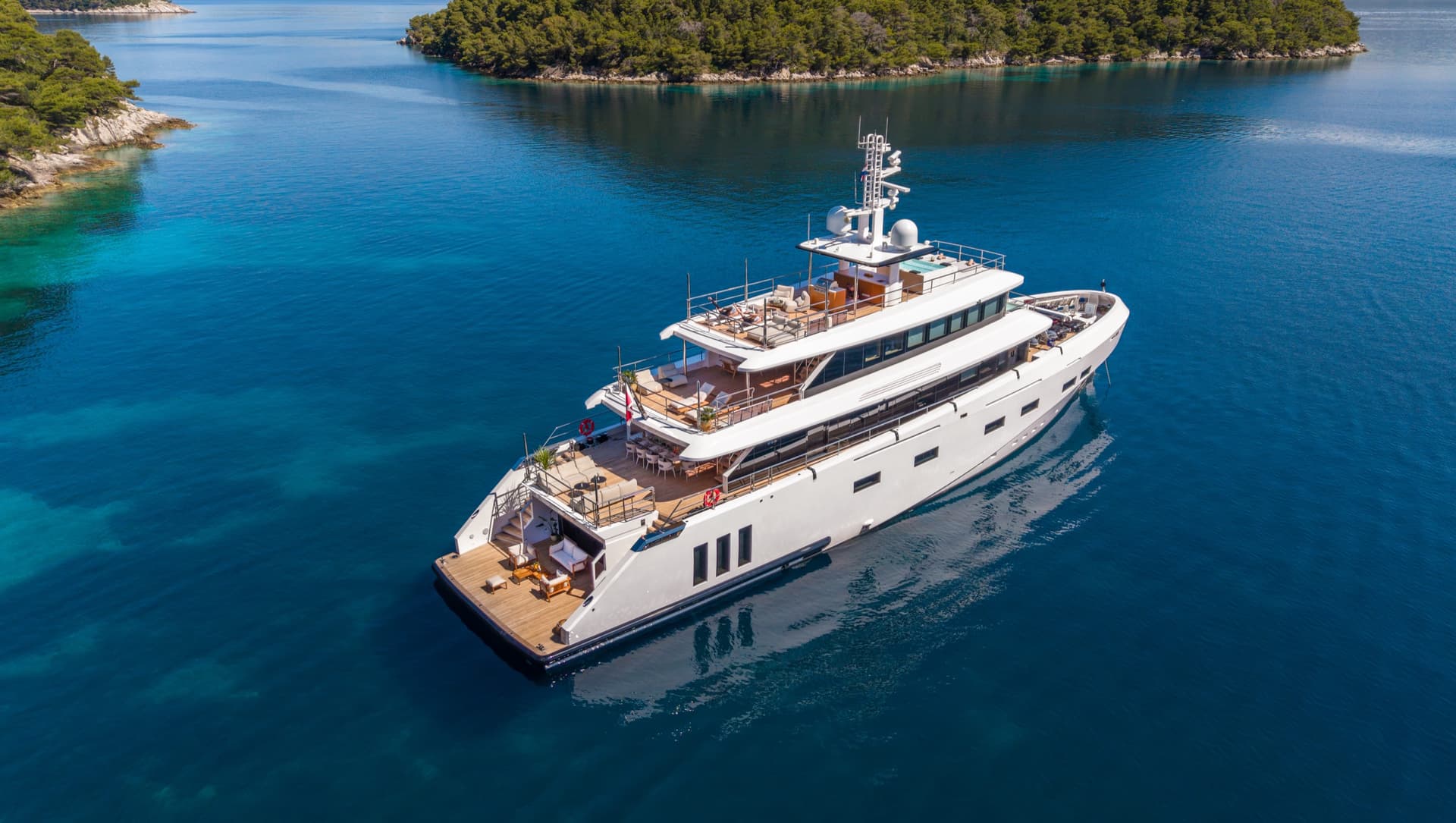 Luxury white yacht anchored in clear blue coastal waters near forested islands