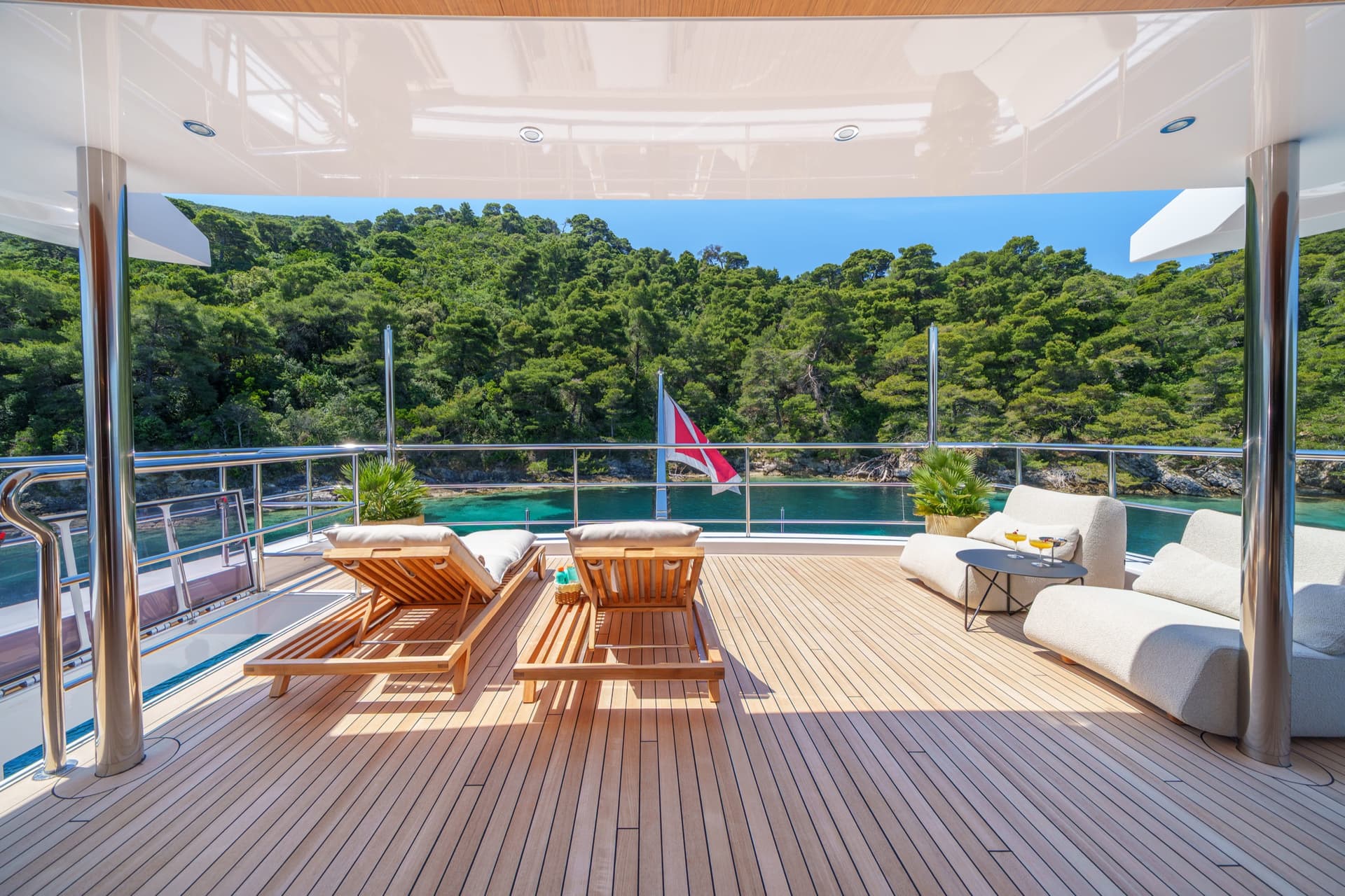 Luxury yacht deck with wooden loungers and seating overlooking a forested coastal bay