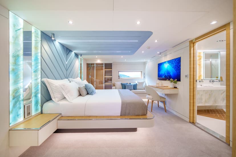 Luxury yacht aft cabin interior with large bed, desk, TV, and attached bathroom.