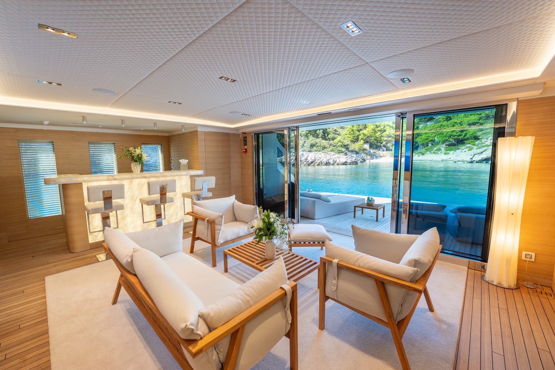 Luxury yacht interior lounge with white seating, bar counter, and open sliding glass doors overlooking the sea
