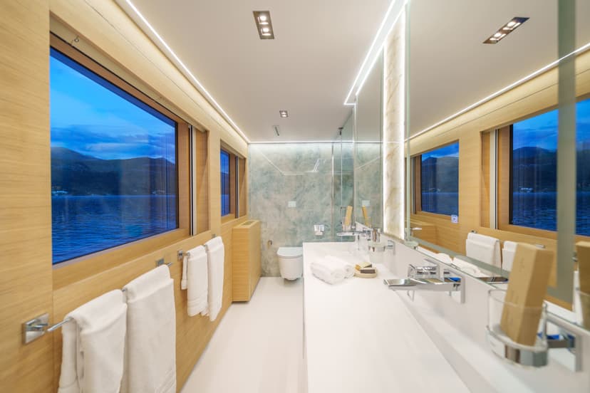 Luxury yacht master cabin bathroom with wooden paneling, large windows overlooking the sea, and a toilet.