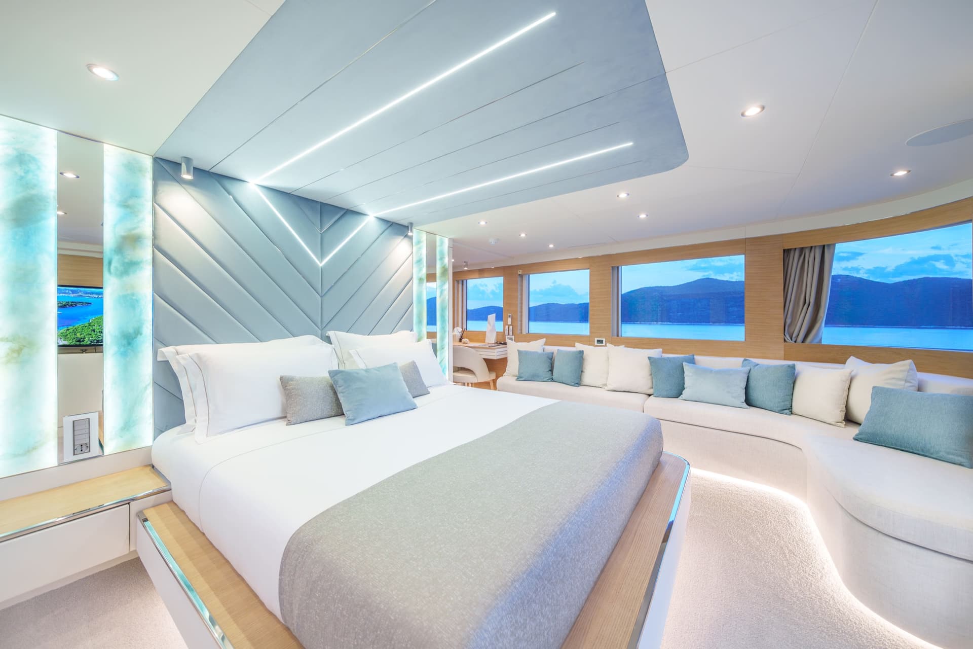 Luxury yacht master cabin with large bed, sofa seating, and coastal windows