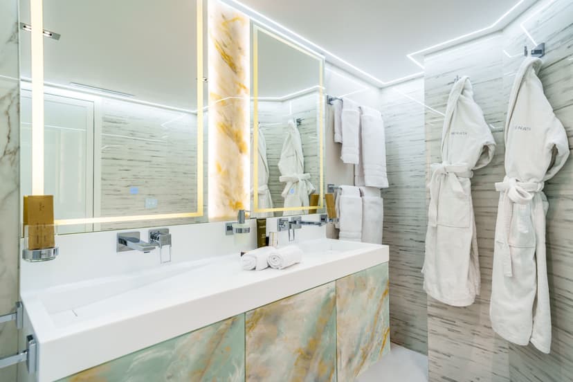 Modern yacht bathroom interior with marble double sinks, illuminated mirrors, and white bathrobes hanging on the wall.