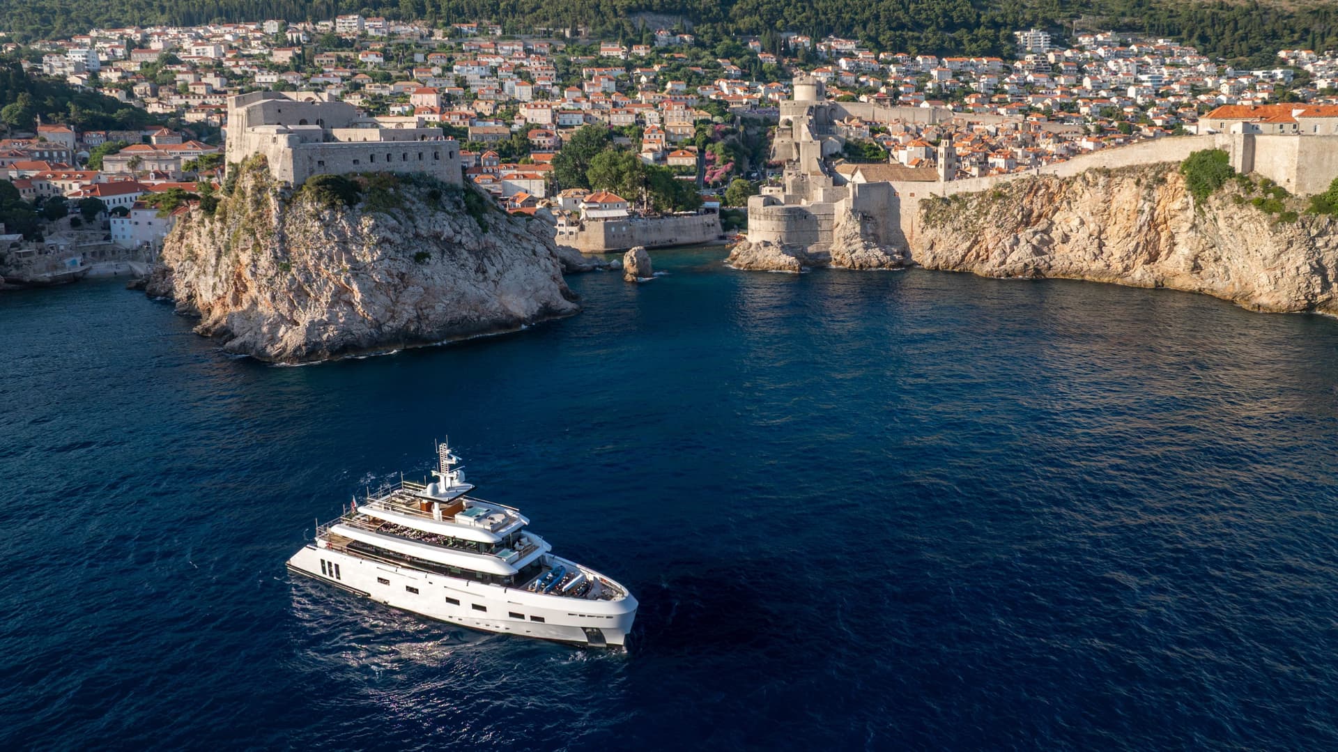 Yacht on blue sea near historic coastal fortress and town with orange tile roofs
