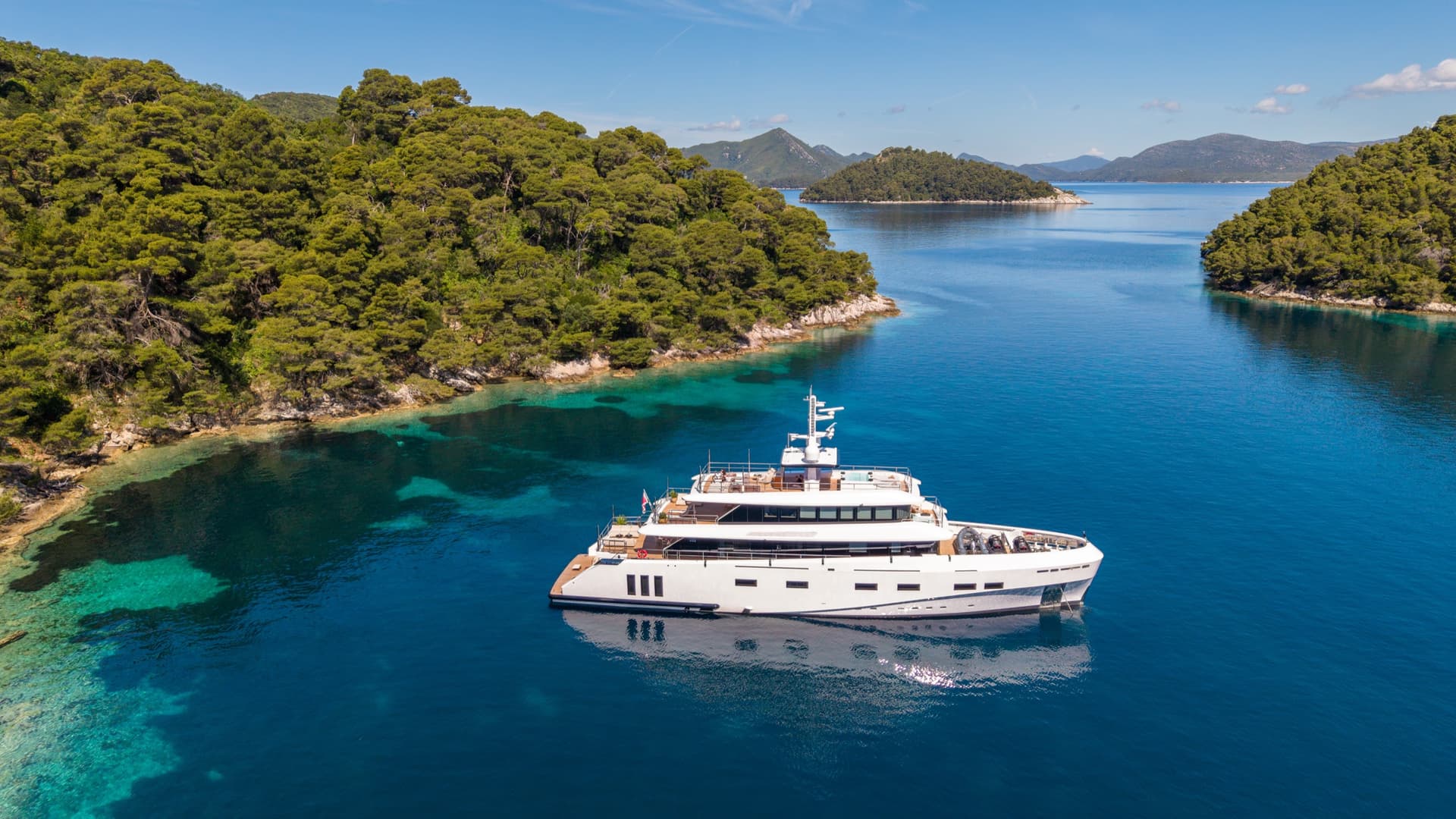 Luxury yacht anchored in a calm bay with turquoise coastal waters and wooded islands
