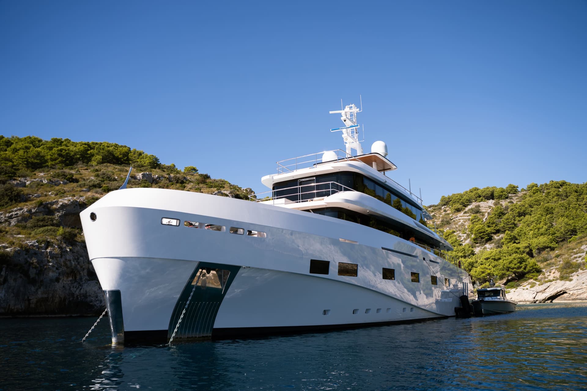 Large white yacht anchored in a coastal cove with green hills under a blue sky