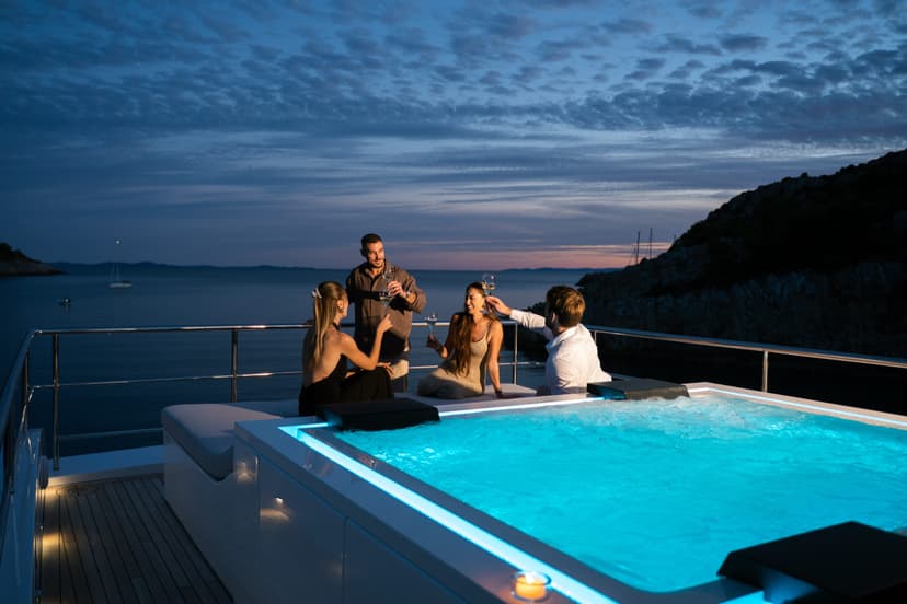 People toasting with wine in a hot tub on a yacht at night with sea and twilight sky background